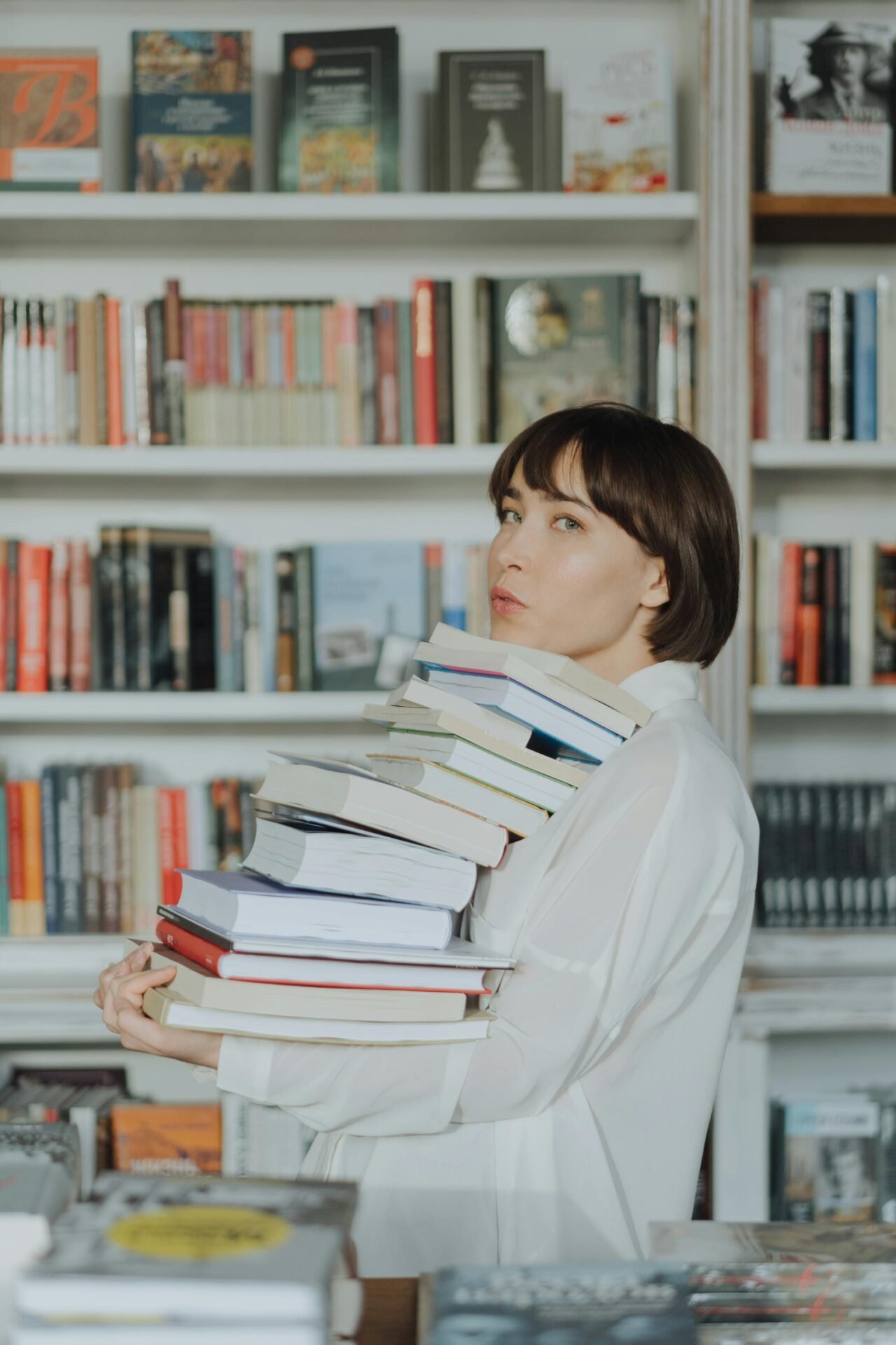 Glückselige Person mit einem hohen Stapel Bücher in einem gemütlichen Buchladen.