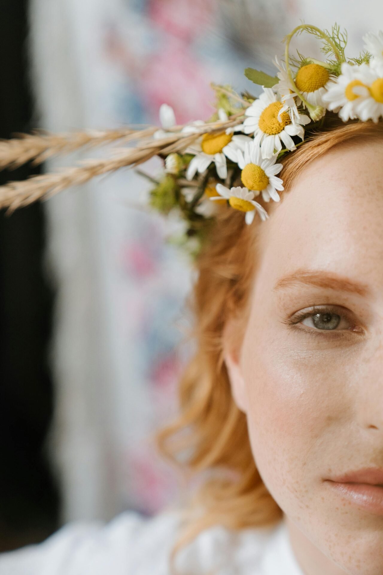 Eine rothaarige Frau schaut freundlich zum Betrachter. Auf ihrem Kopf liegt ein Kranz aus Margeriten und Kornblumen. Sie wirkt skandinavisch, wie Astrid Lindgren.