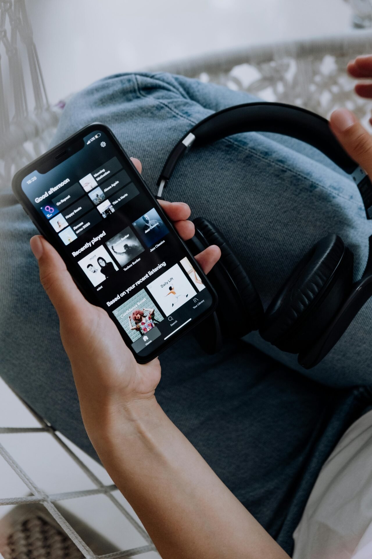 Person hält ein Smartphone mit geöffneter „Musik zur Konzentration“-Playlist und Kopfhörer auf dem Schoß.