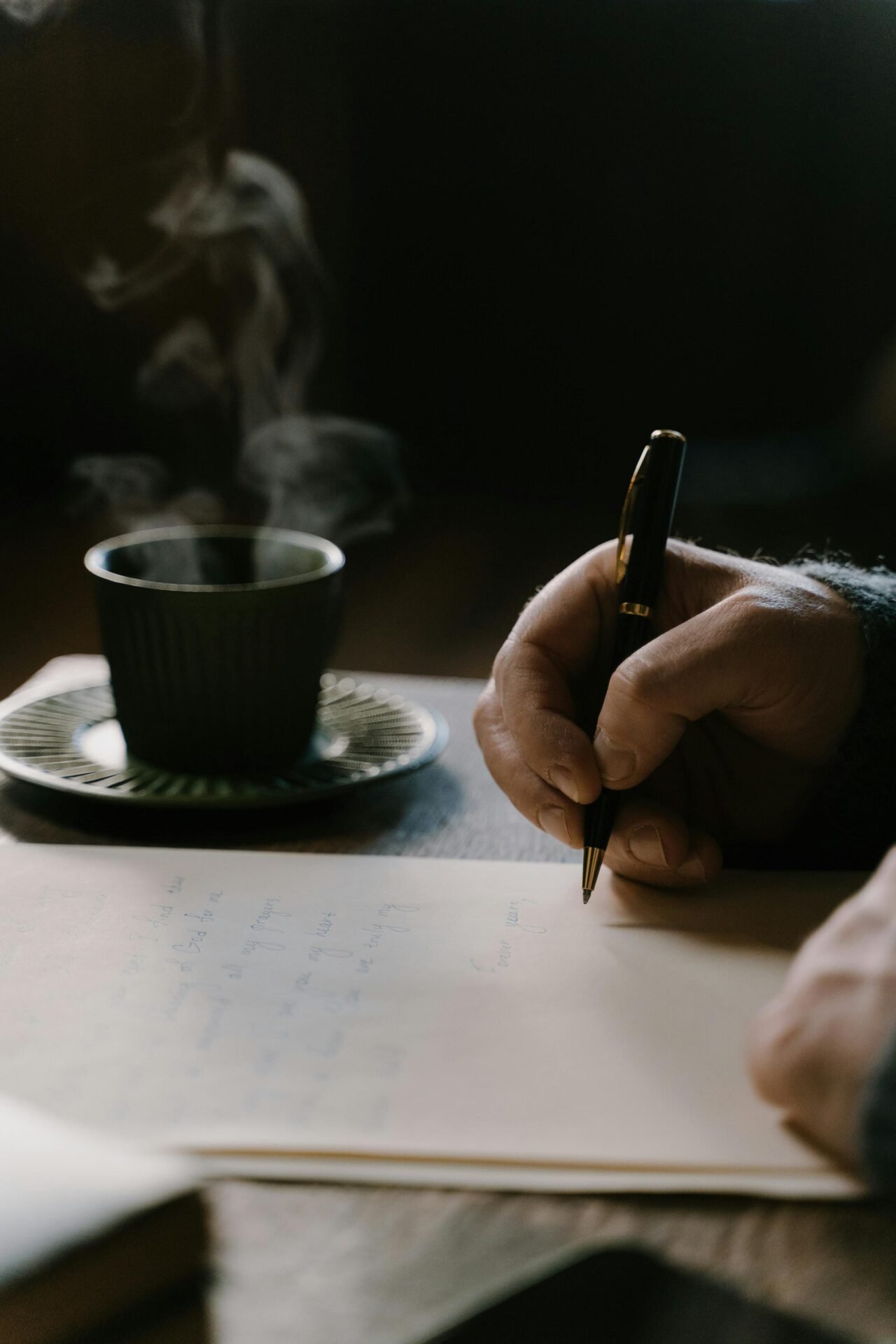 Eine Person schreibt mit einem Stift und stellt sich neben einer dampfenden Tasse Kaffee ihr Zukunfts-Ich vor.