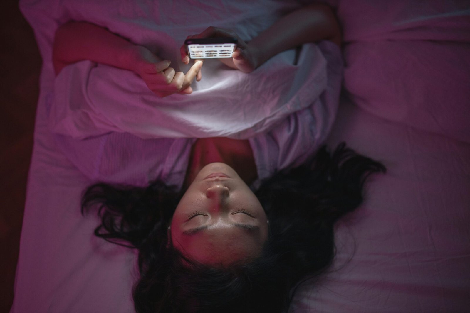Person, die nachts im Bett liegt, auf dem Telefon scrollt und eine 5-Uhr-Morgenroutine plant.