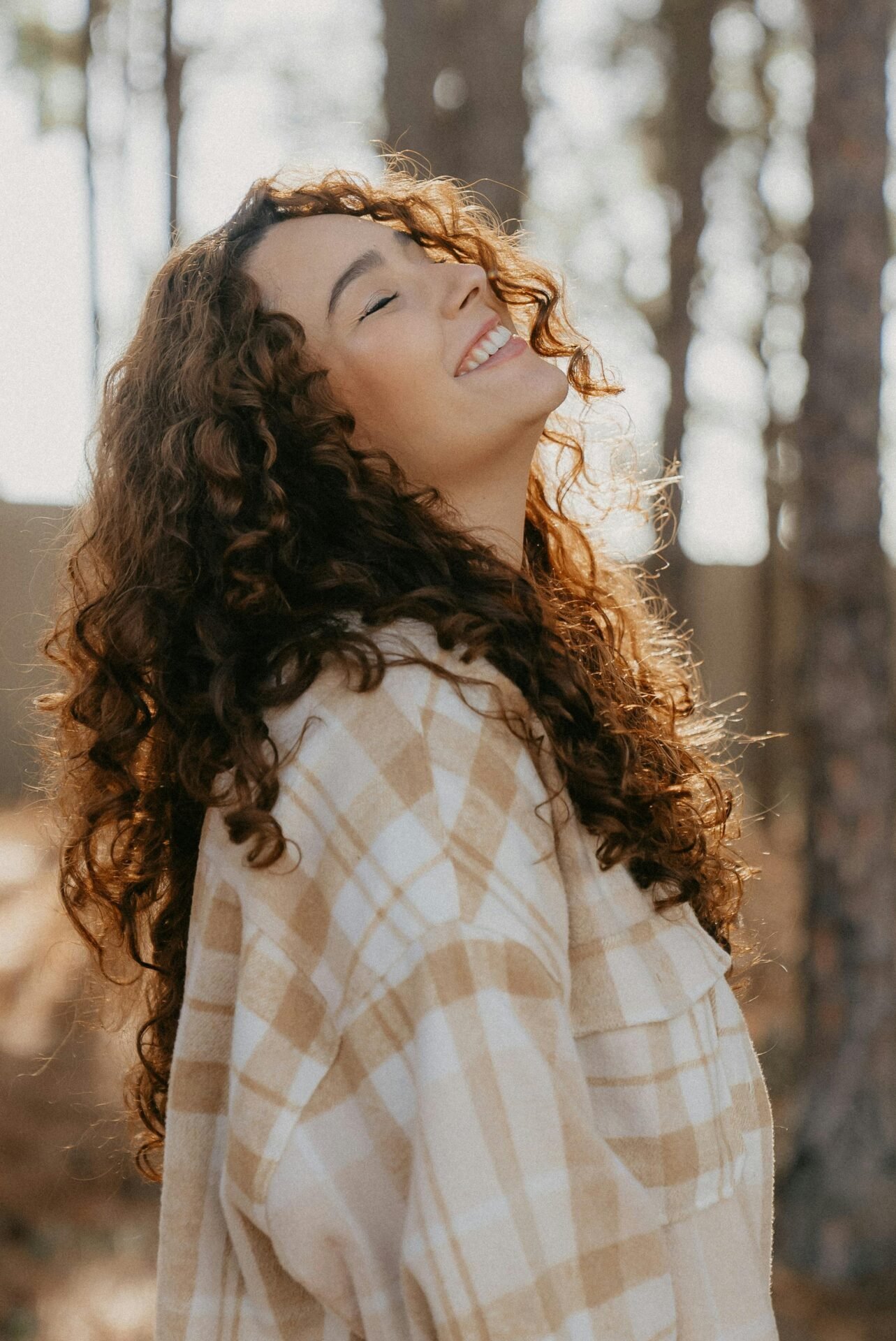 Eine Frau mit dunklen Locken und einem karierten Hemd reckt glücklich das Gesicht gen Sonne.