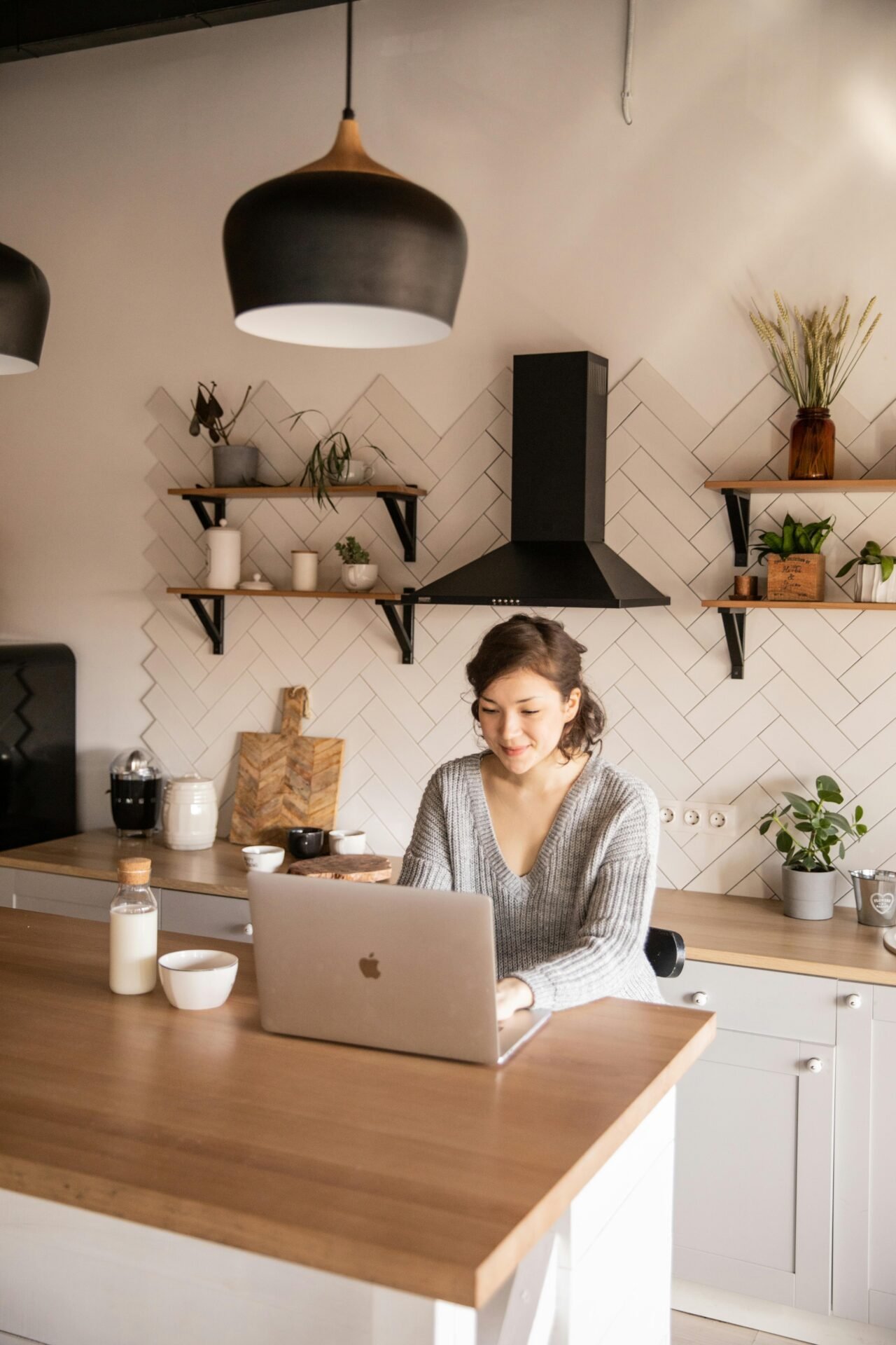 Eine junge Frau sitzt in der Küche zufrieden an einem Laptop und arbeitet - vielleicht während ihrer 5-Uhr-Morgenroutine.