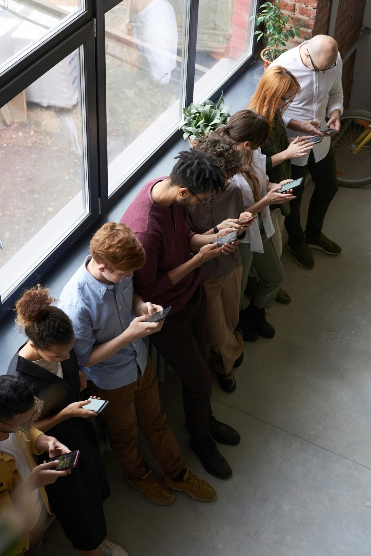 Sieben Menschen stehen drinnen in einer Reihe, ihre Smartphones als zeitfresser im Alltag.