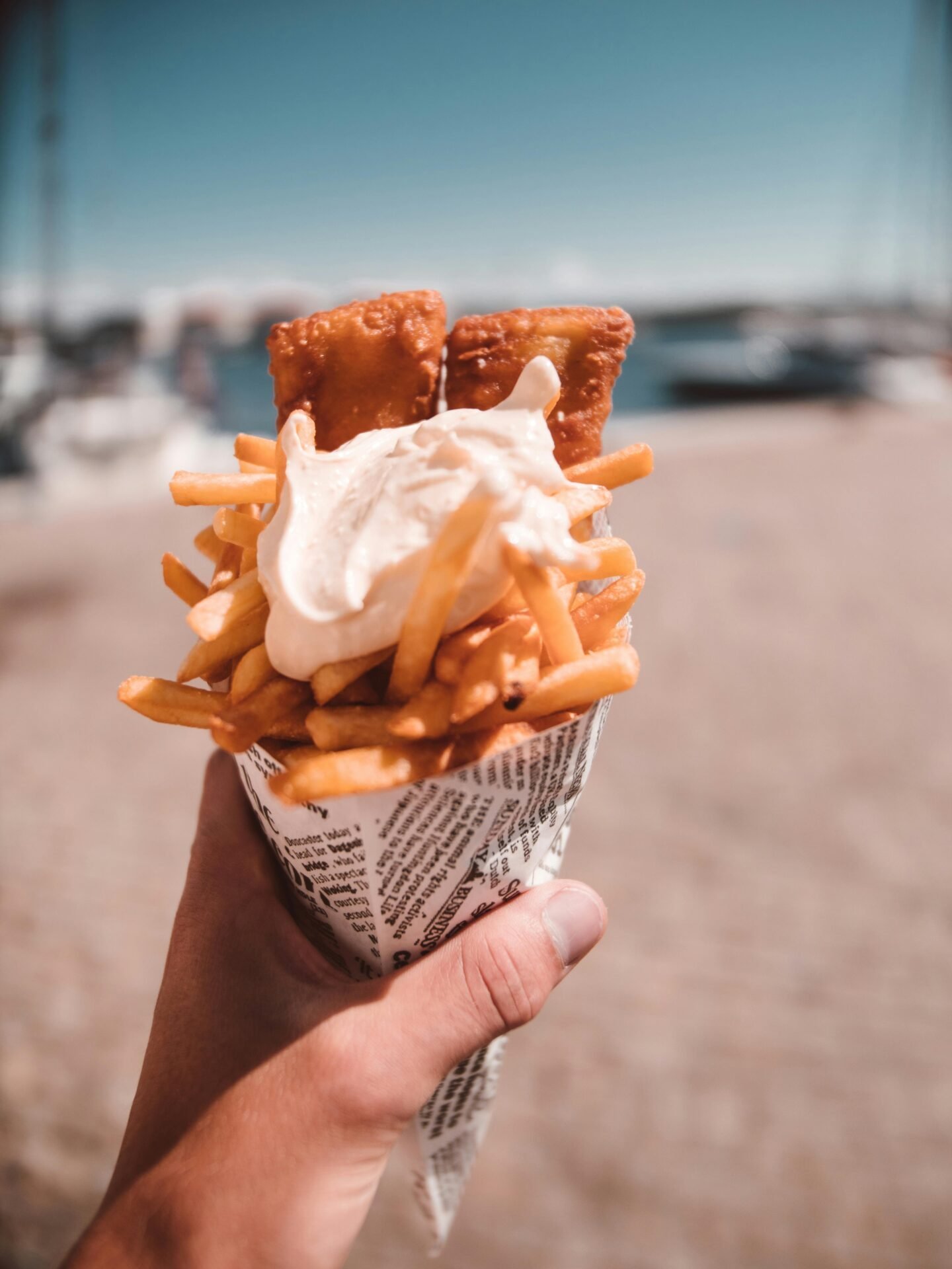 In der Hand eine Tüte mit Pommes, Fischstäbchen und Soße – Streetfood trifft im Freien auf gesunden Lebensstil.