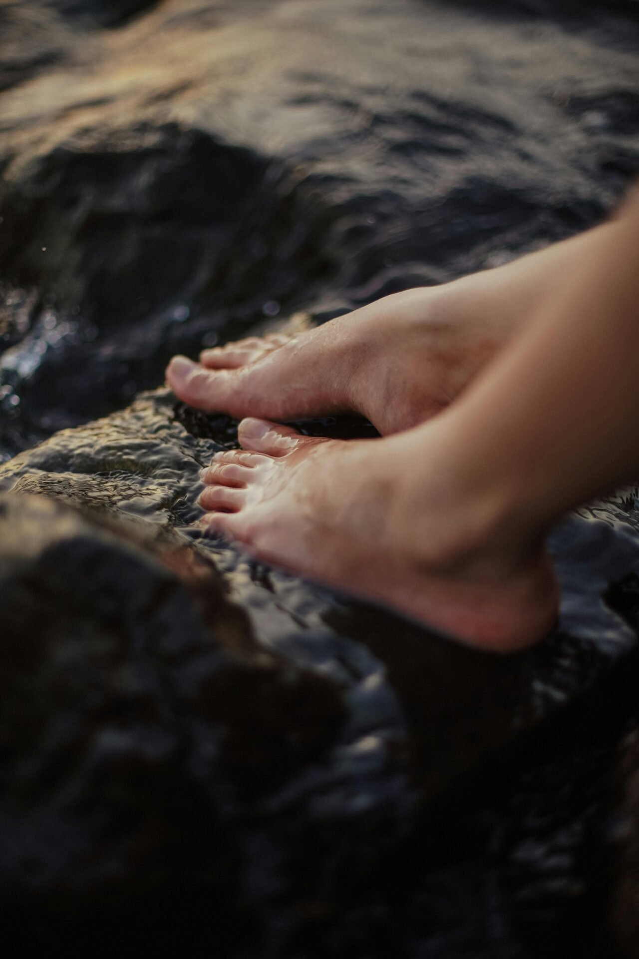 Nackte Füße auf nassen, dunklen Steinen am Wasser – ein Moment des gesunden Lebens.