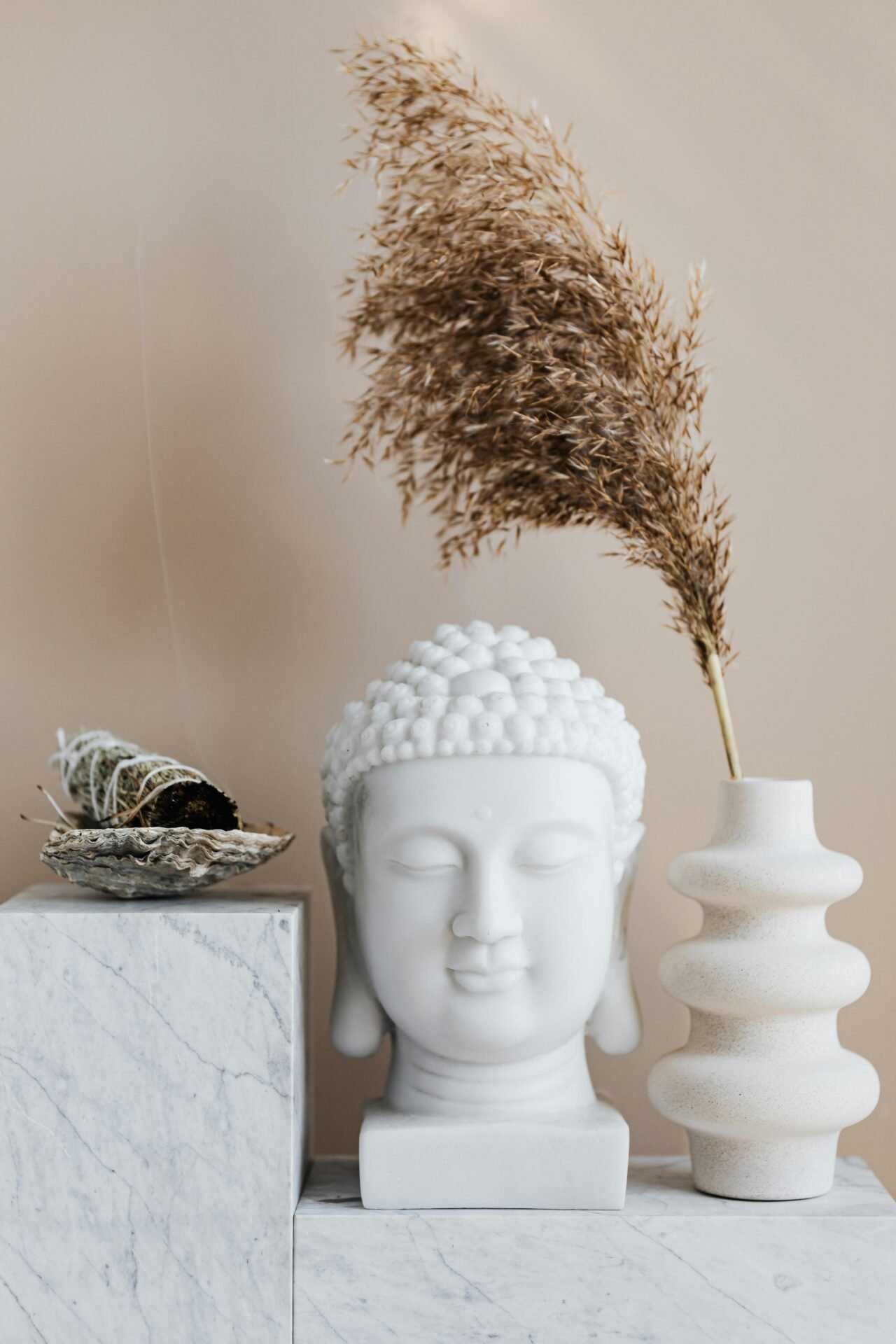 Weiße Buddhakopfstatue, Vase mit getrockneten Pflanzen und Salbeibündel für Weisheit auf Marmoroberfläche.