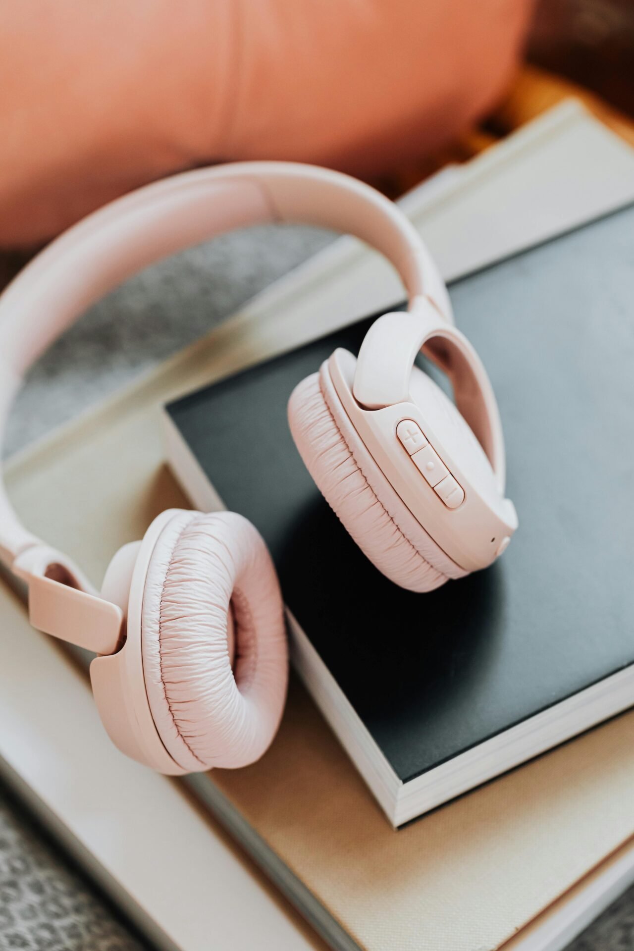 Rosafarbene kabellose Kopfhörer für konzentrierte Musik liegen auf einem Stapel Bücher und Notizbücher.