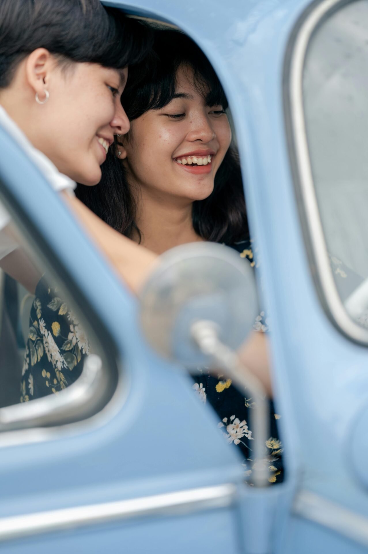 Gemeinsam erfolgreich: Zwei Menschen lächeln in einem blauen Oldtimer durch das Fenster.