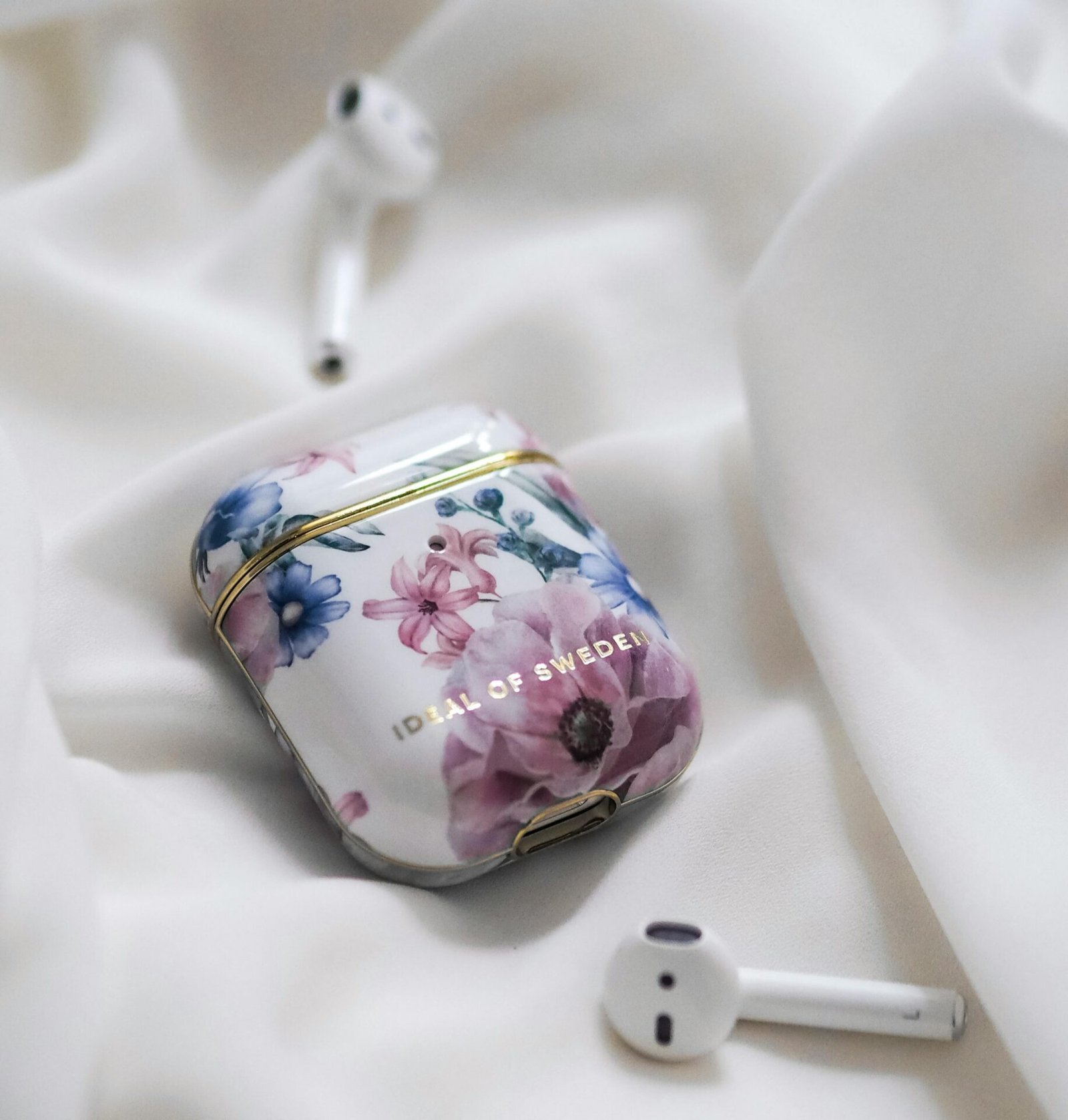AirPods in einem Case mit Blumenmuster auf einem weißen Tuch.