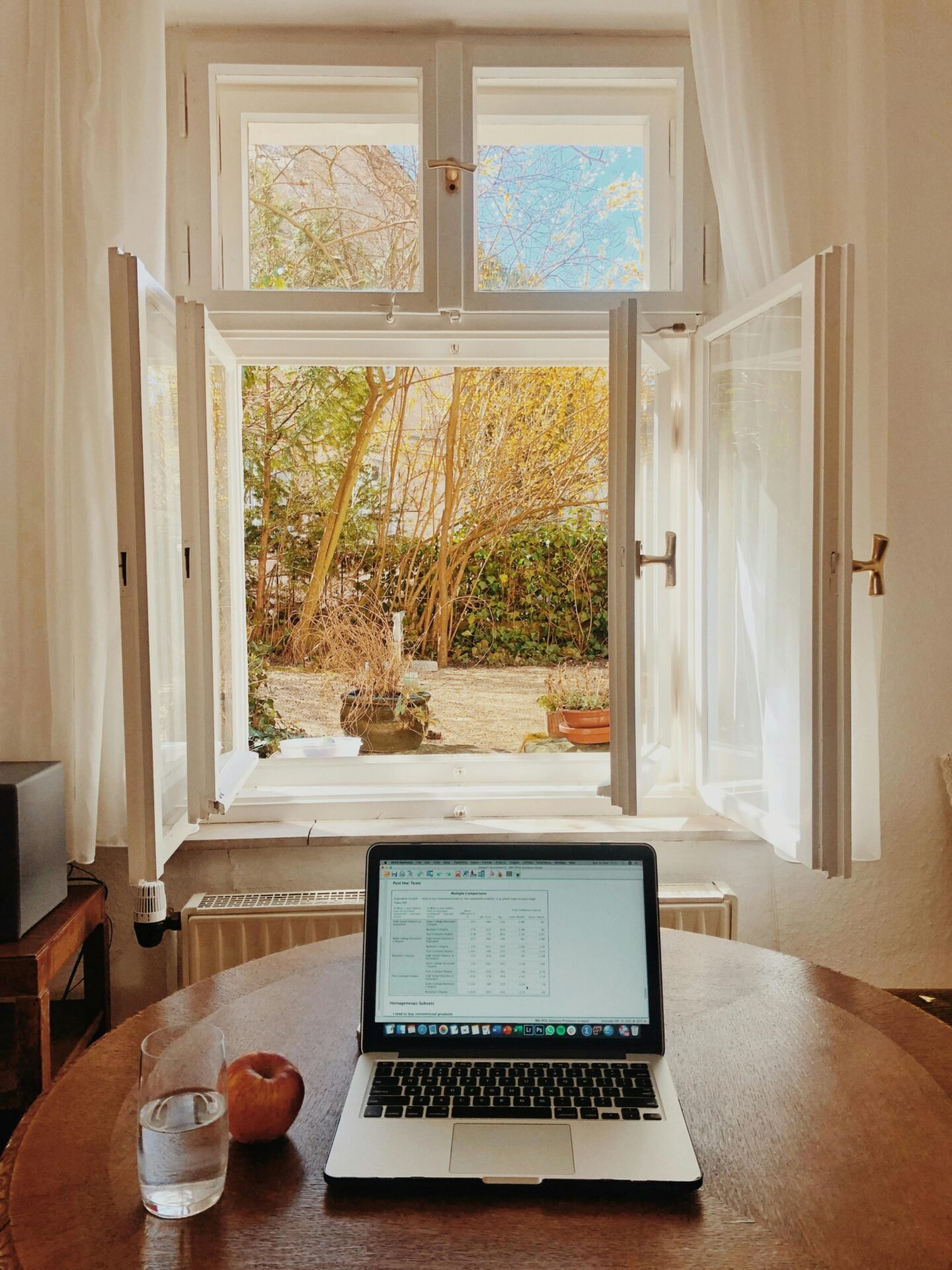 Laptop, Apfel und Glas Wasser auf dem Tisch – Prioritäten setzen am offenen Fenster mit Blick in den Garten.