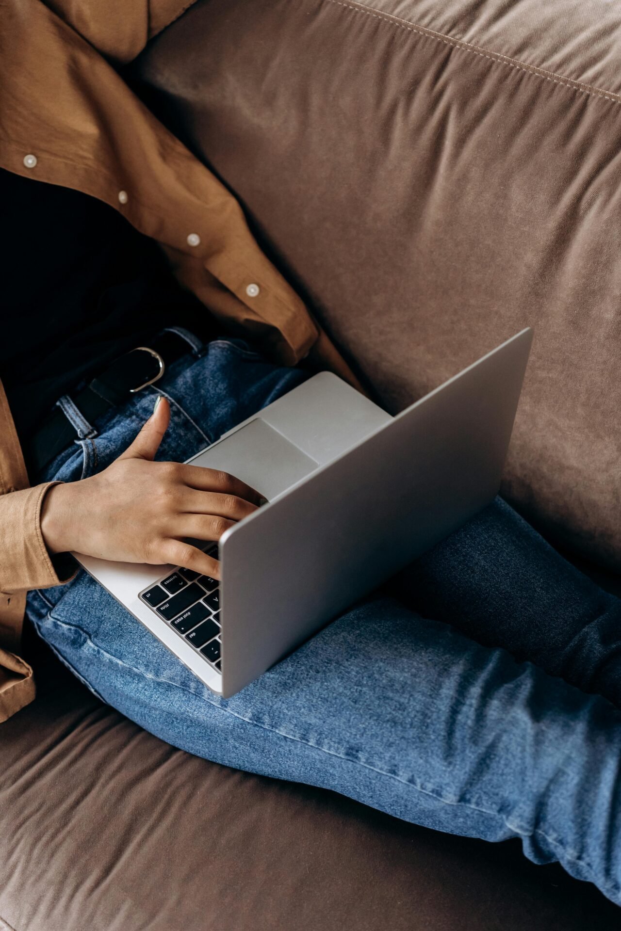 Person in Jeans und brauner Jacke, die auf einer Couch sitzt und einen Laptop benutzt – Zukunftspläne plant.