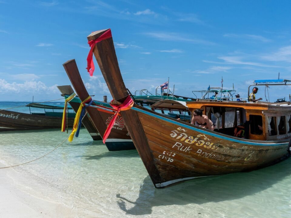Am Strand liegen Langheckboote mit bunten Bändern, die eine Mai-Pen-Rai-Atmosphäre verkörpern.