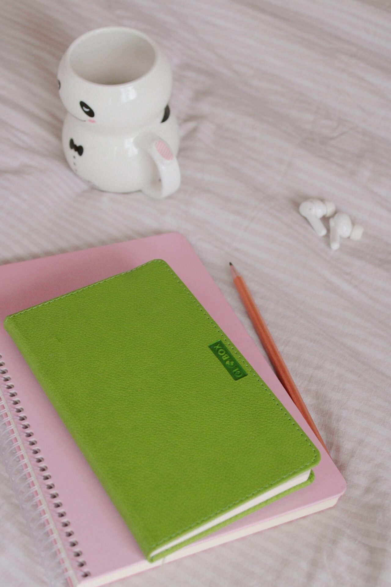 Zwei Notizbücher auf einem Bett mit Airpods und einer Tasse - Equipment zum Lebensziel finden.