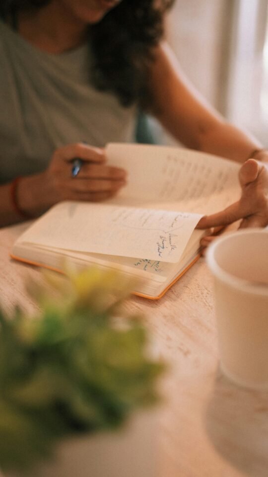 Schreiben Sie in ein Notizbuch, um Ihre Handschrift zu verbessern, und stellen Sie dabei eine Pflanze und eine Tasse in die Nähe.