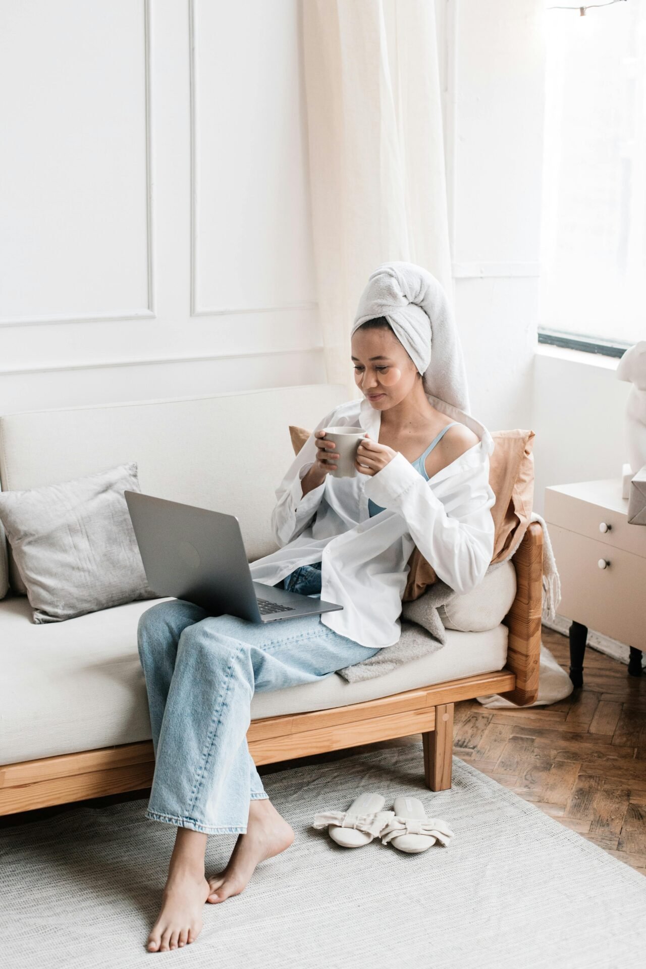 Eine Frau sitzt gemütlich auf deim Sofa mit einer Tasse Kaffee und einem Laptop, um sich für ihr Vision Board inspirieren zu lassen.