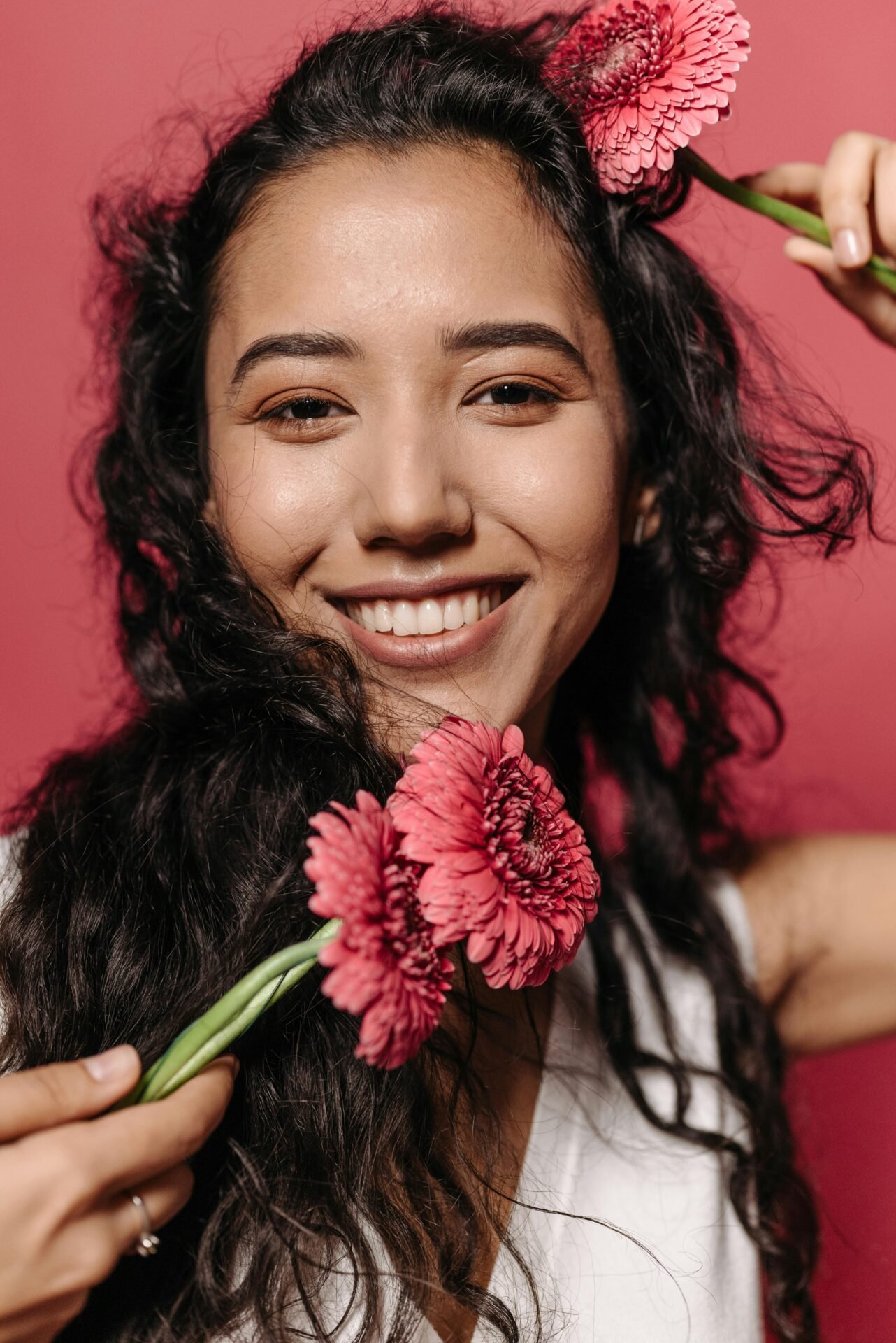 Eine fröhliche Frau mit gebräunter Haut, dunklen Augen und dunklen Locken hält pinke Blumen - sie ist glücklich, weil sie ihr Lebensziel gefunden hat.