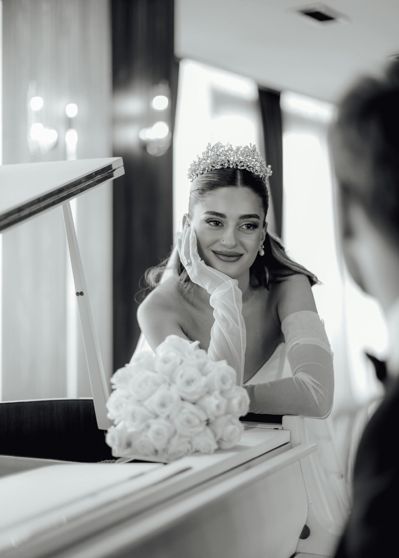 Die Braut im Brautkleid und mit Tiara lächelt den Bräutigam am Klavier an und träumt von ihrer gemeinsamen Zukunft.