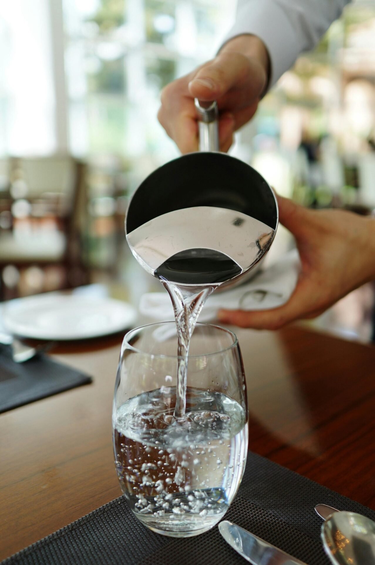 Jemand gießt Wasser in ein Glas - wie das, was man morgens trinken sollte, um wach zu werden.