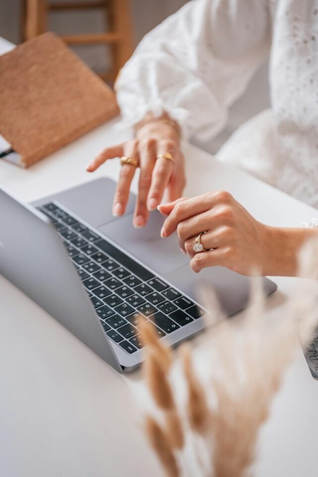 Eine Person tippt auf einem Laptop, Notizbücher stehen in der Nähe und stellt sich ihr zukünftiges Ich am weißen Schreibtisch vor.