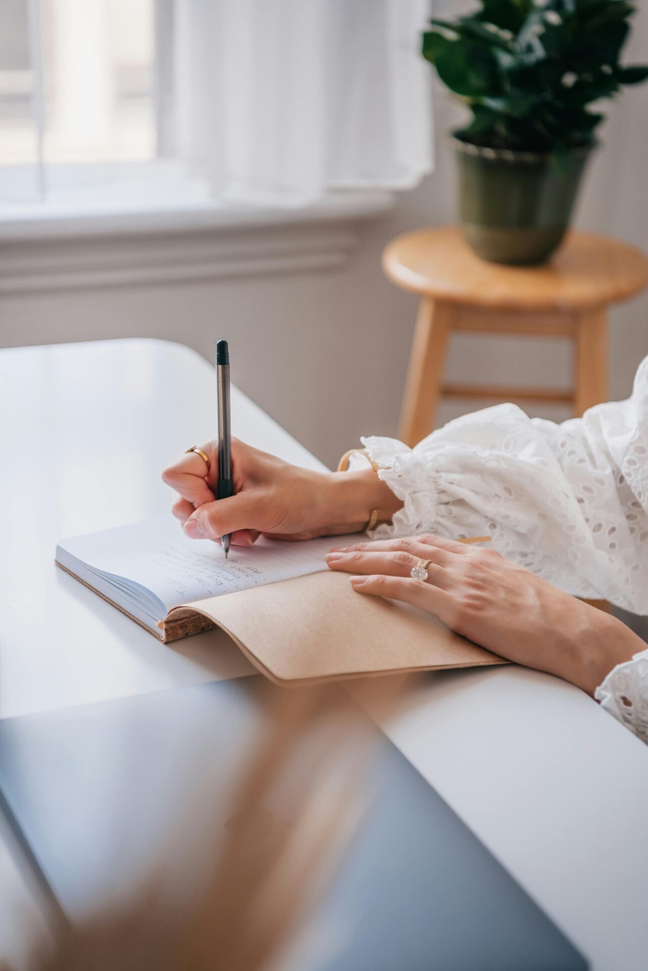 Person, die an einem Schreibtisch in ein Journal schreibt für eine gesunde Psyche, im Hintergrund eine Pflanze.