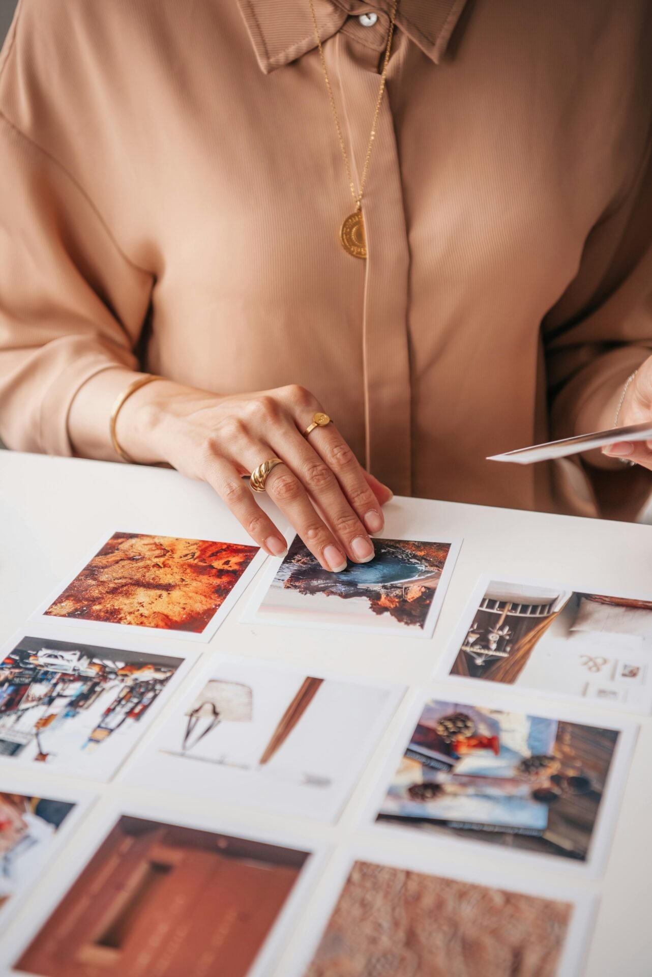 Eine Frau mit goldenen Ringen und einer beigen Bluse sortiert auf einem Tisch Fotos.