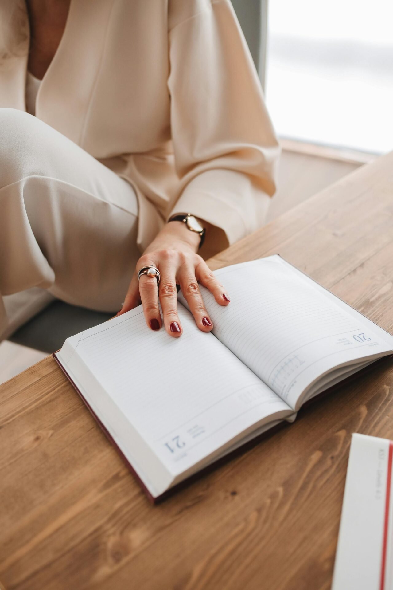 Person mit roten Nägeln und Ringen ruht mit der Hand auf dem Planer und fängt kleine Glücksmomente ein.