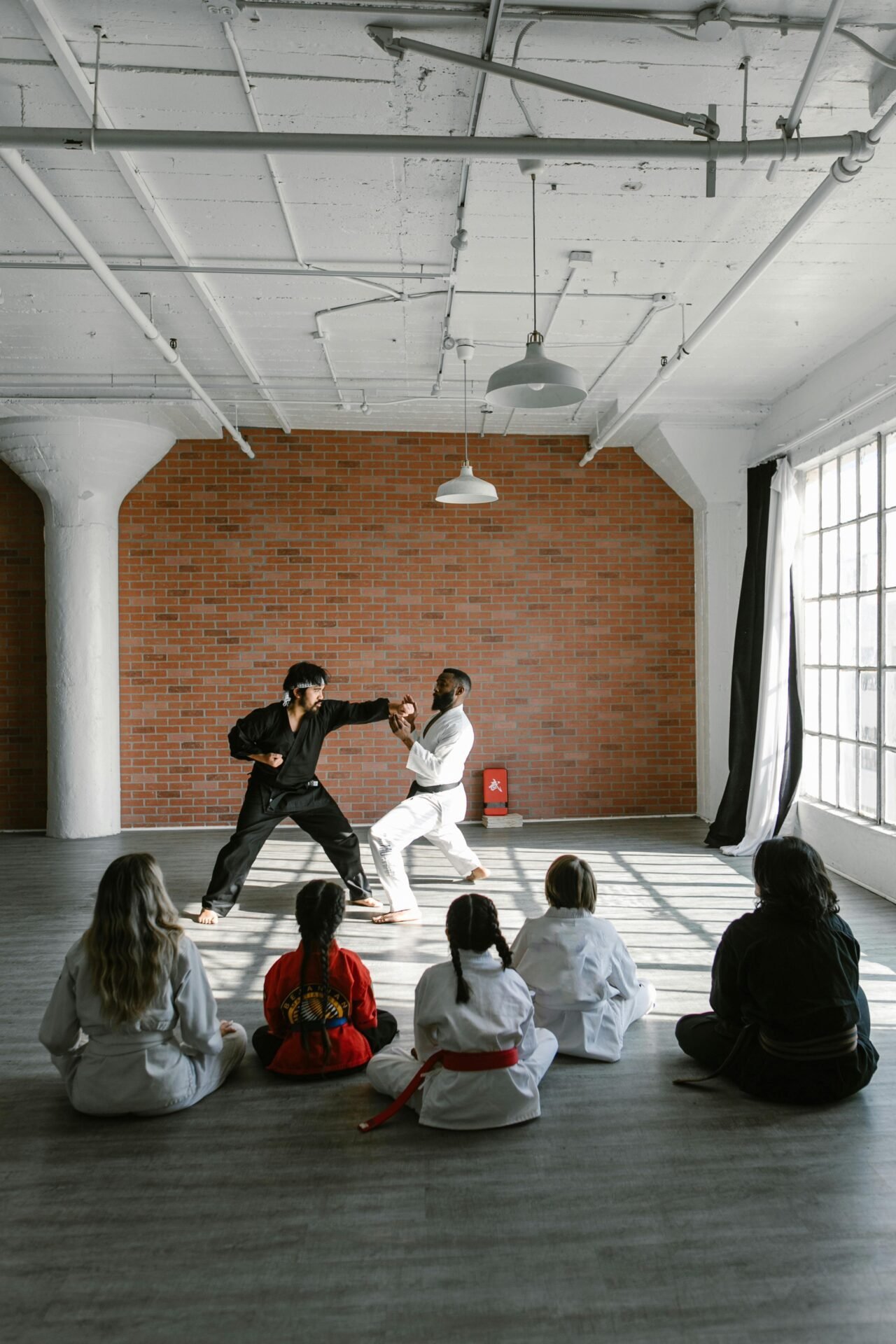 Ein Dojo, in dem zwei Männer etwas vormachen, während einige Schüler im Sitzen zusehen.