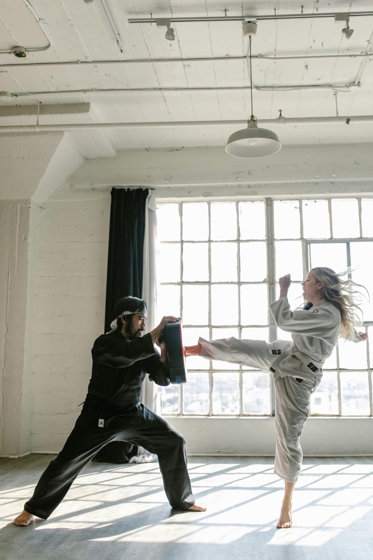 Ein Mädchen tritt gegen eine Fläche, die ein Mann hält. Sie trainiert wohl Taekwondo.