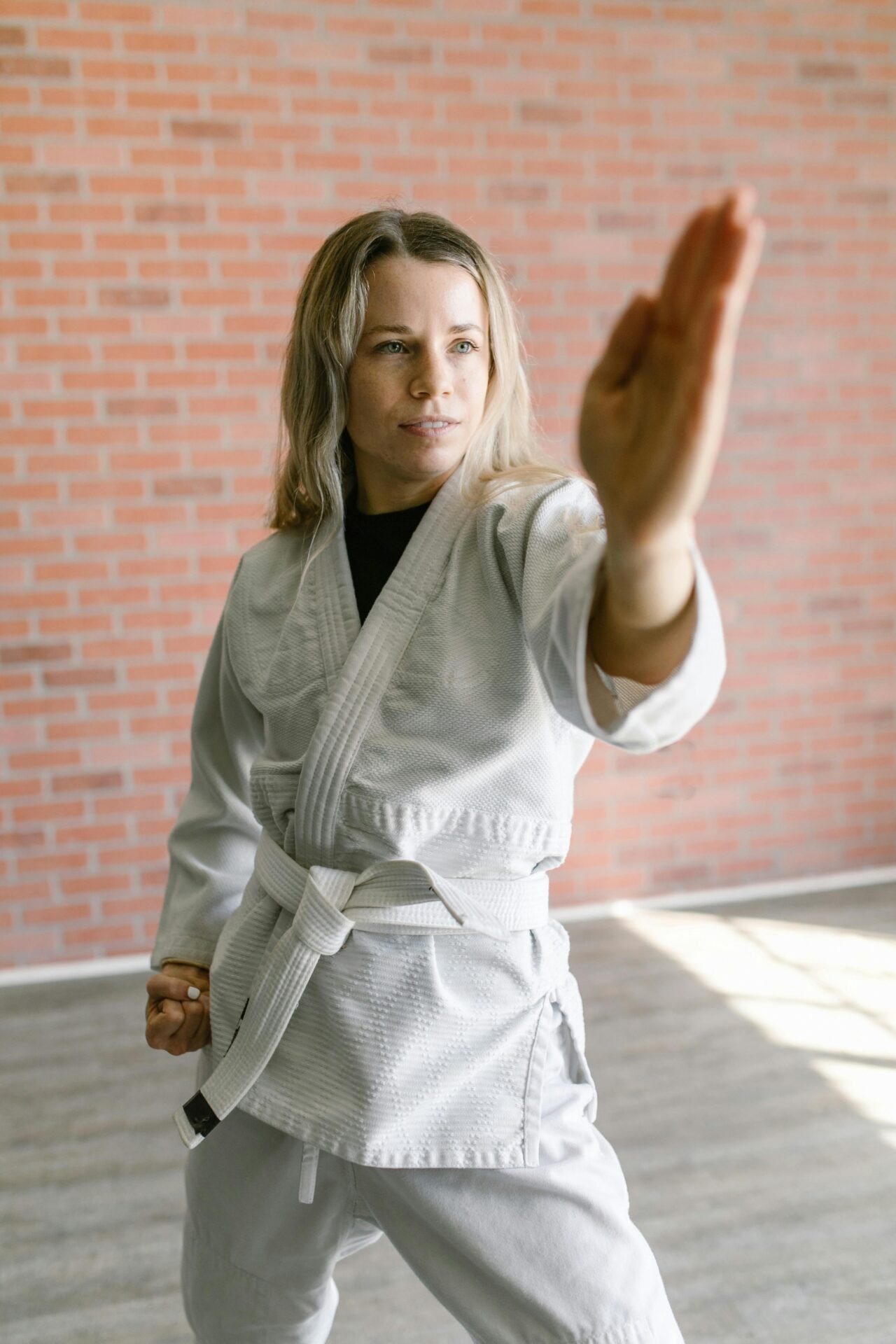 Eine blonde Frau in Judo-Outfit mit weißem Gürtel steht in Verteidigungshaltung.