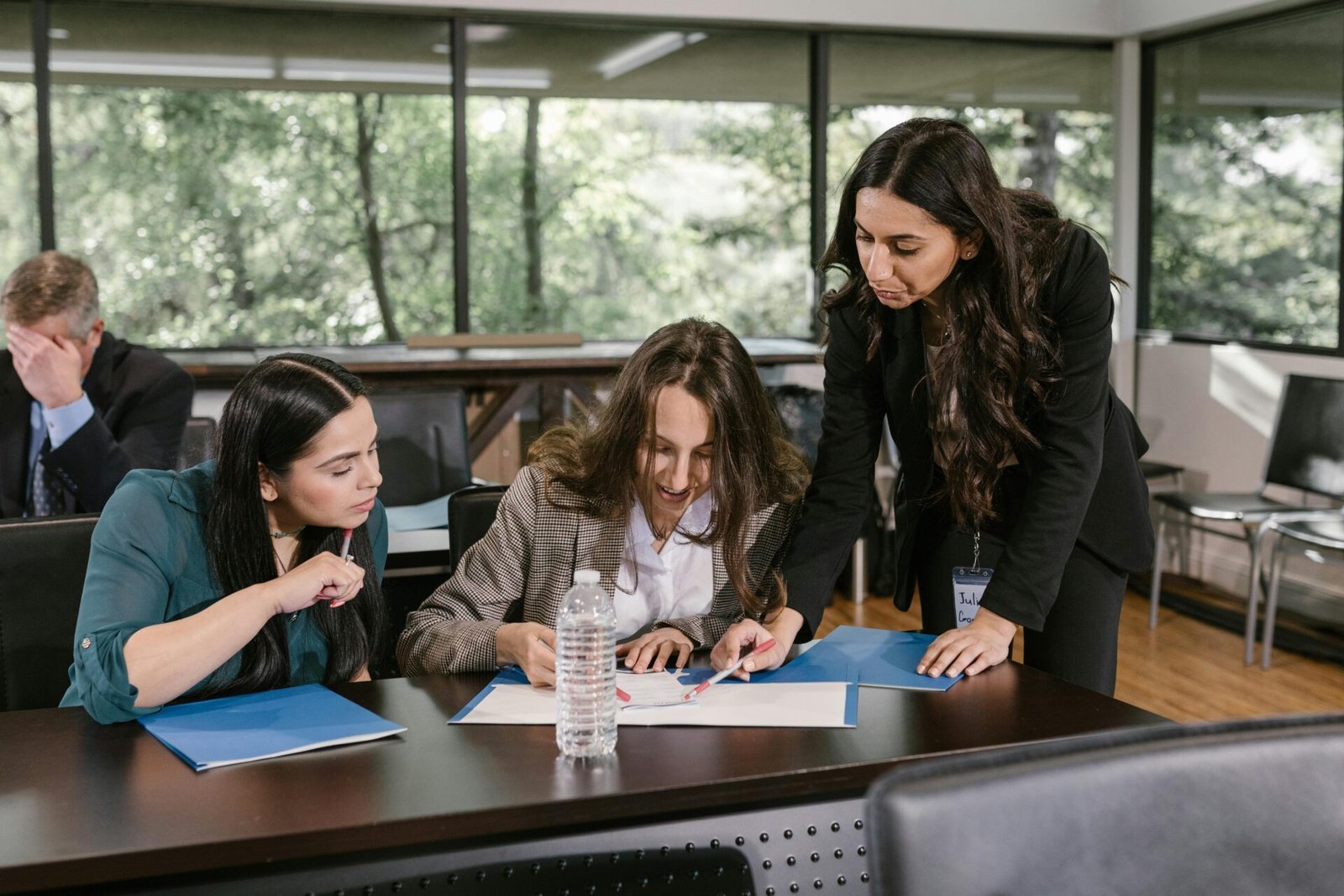 Drei Frauen erledigen in einem hellen Büro mit großen Fenstern gemeinsam Papierkram und besprechen die Arbeit in den USA.
