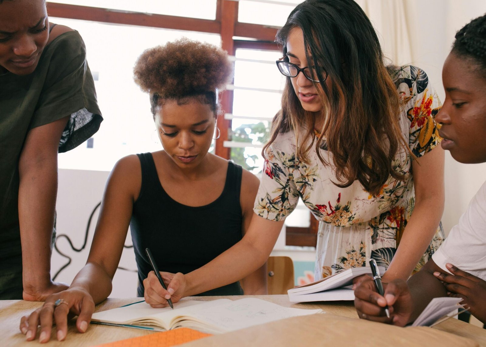 Vier Frauen mit starker Persönlichkeit arbeiten zusammen, schreiben und besprechen gemeinsam Notizen.