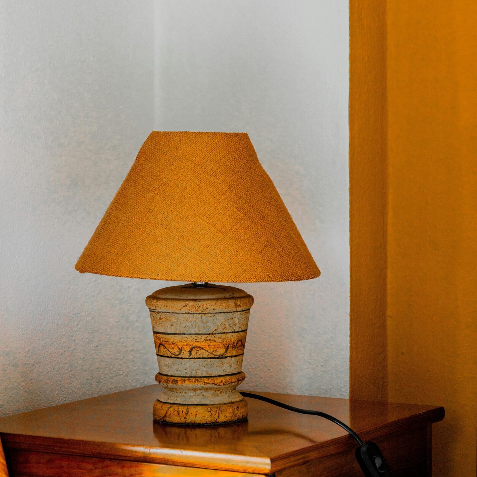 Eine warme, orangefarbene Lampe mit einem Standfuß aus Ton, die auf einer hölzernen Kommode steht und eine gemütliche Atmosphäre schafft.