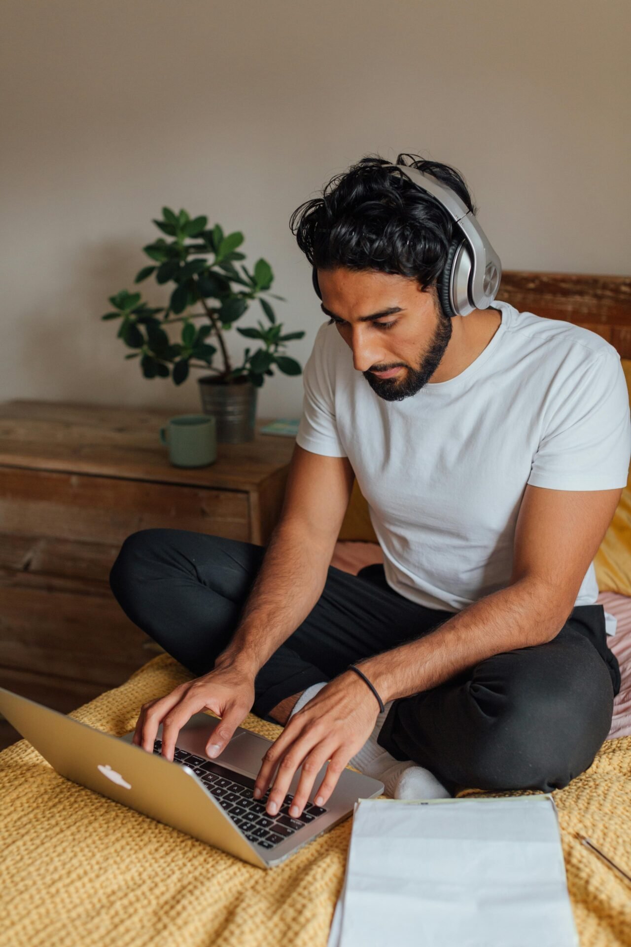 Ein Mann sitzt im Schneidersitz auf dem Bett, arbeitet konzentriert am Laptop und hört dabei Musik.