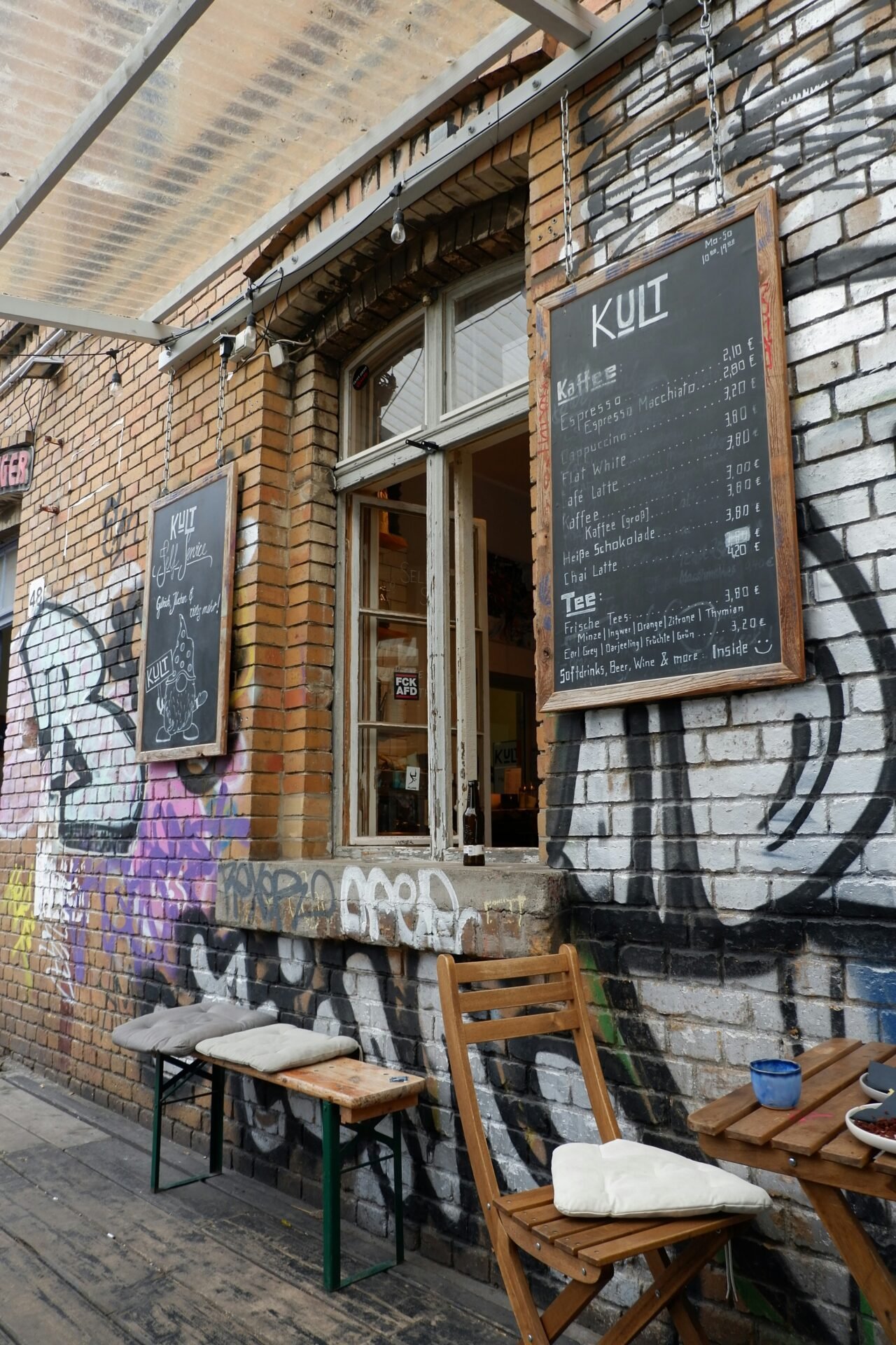 Außencafé in der Nähe der Berliner Sehenswürdigkeiten, mit Speisekarten auf Kreidetafeln, Bänken und Graffiti-Wänden.