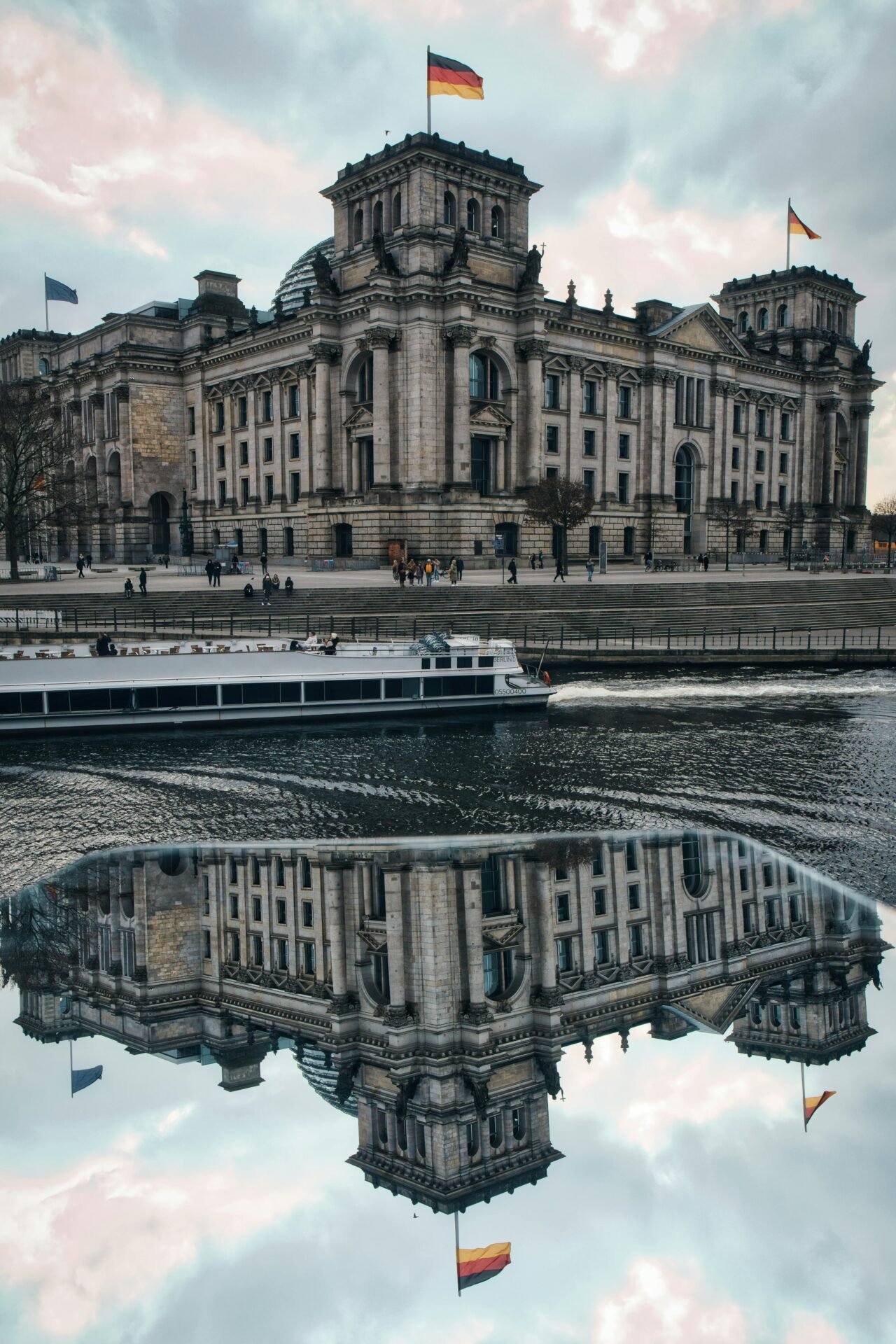Historisches Steingebäude, eine Berliner Sehenswürdigkeit, spiegelt sich in einem Fluss mit einem vorbeifahrenden Boot.