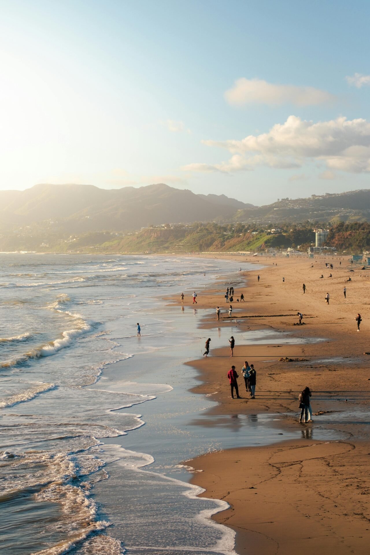 Menschen, die am Sandstrand entlang spazieren, Wellen und Berge – eine Reise ins Glück bei Sonnenuntergang.