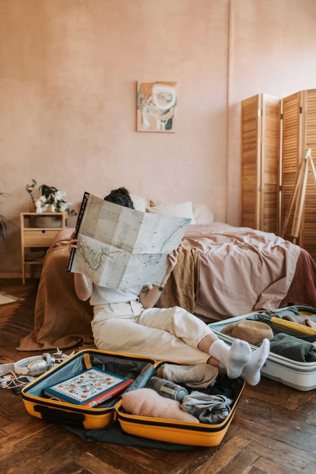 Person sitzt mit offenen Koffern auf dem Boden und plant eine Reise ins Glück in einem gemütlichen Schlafzimmer.