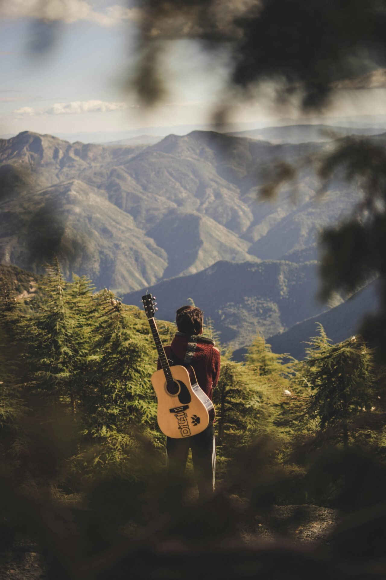 Eine Person mit einer Gitarre steht zwischen Bäumen und blickt auf ihrer Reise ins Glück auf einen malerischen Berg.